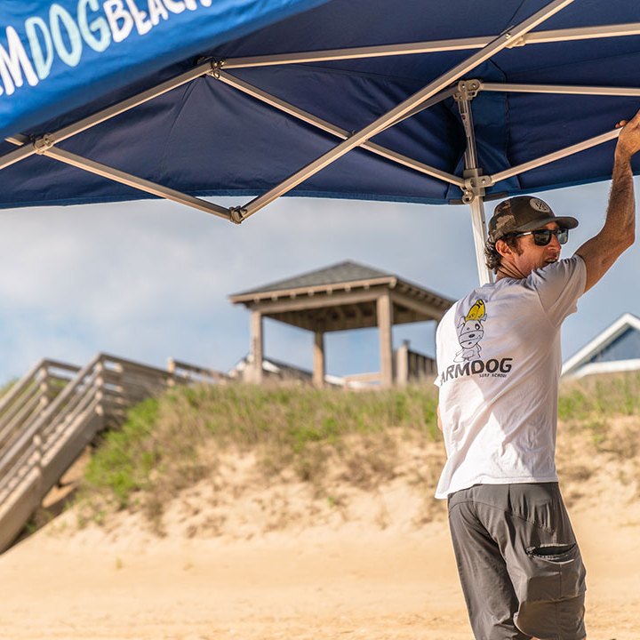 a man working for Farmdog Beach Services setting up a beach tent on a sandy beach