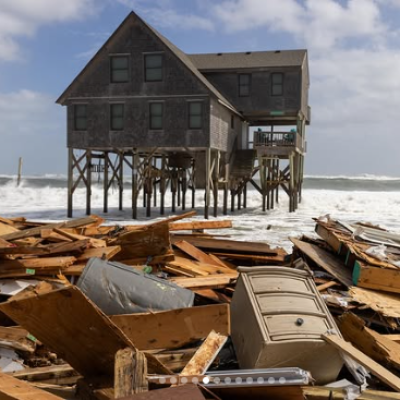 Coastal house on stilts with debris scattered on beach after storm