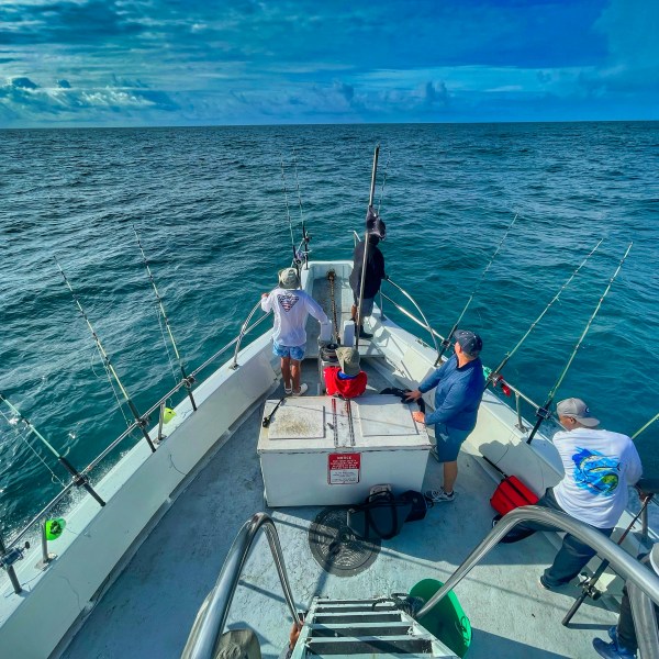 People fishing on a boat at sea with blue sky and clouds above.