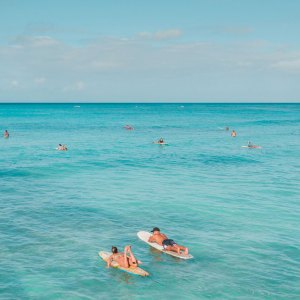 Surfers on blue ocean water under a clear sky, lying on surfboards.