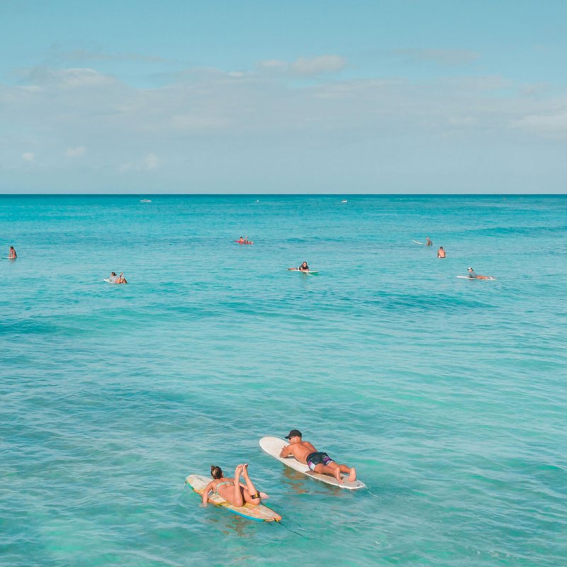 Surfers on blue ocean water under a clear sky, lying on surfboards.