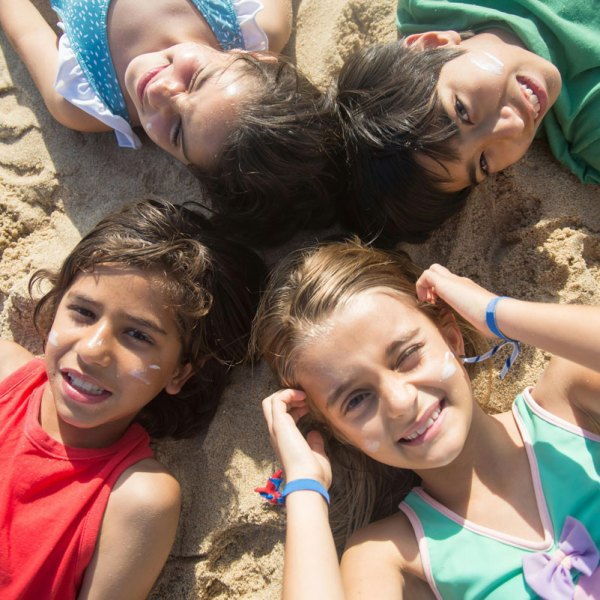 Four children lying in a circle on sandy beach, smiling.