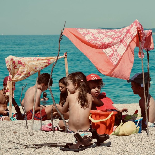 Children playing under makeshift tents on a sandy beach by the sea.