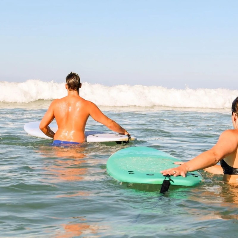 Two surfers with boards wade into the ocean towards approaching waves.