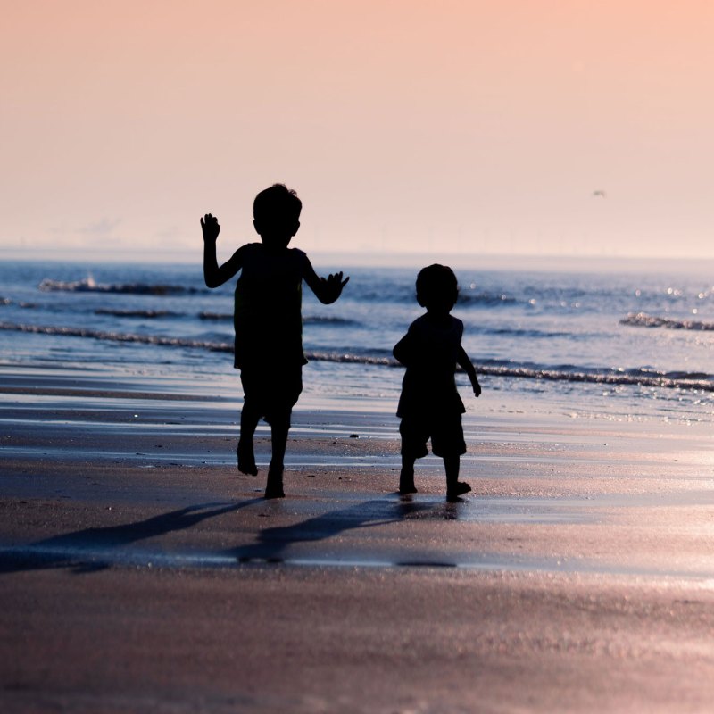 Silhouettes of two children running on a beach at sunset.